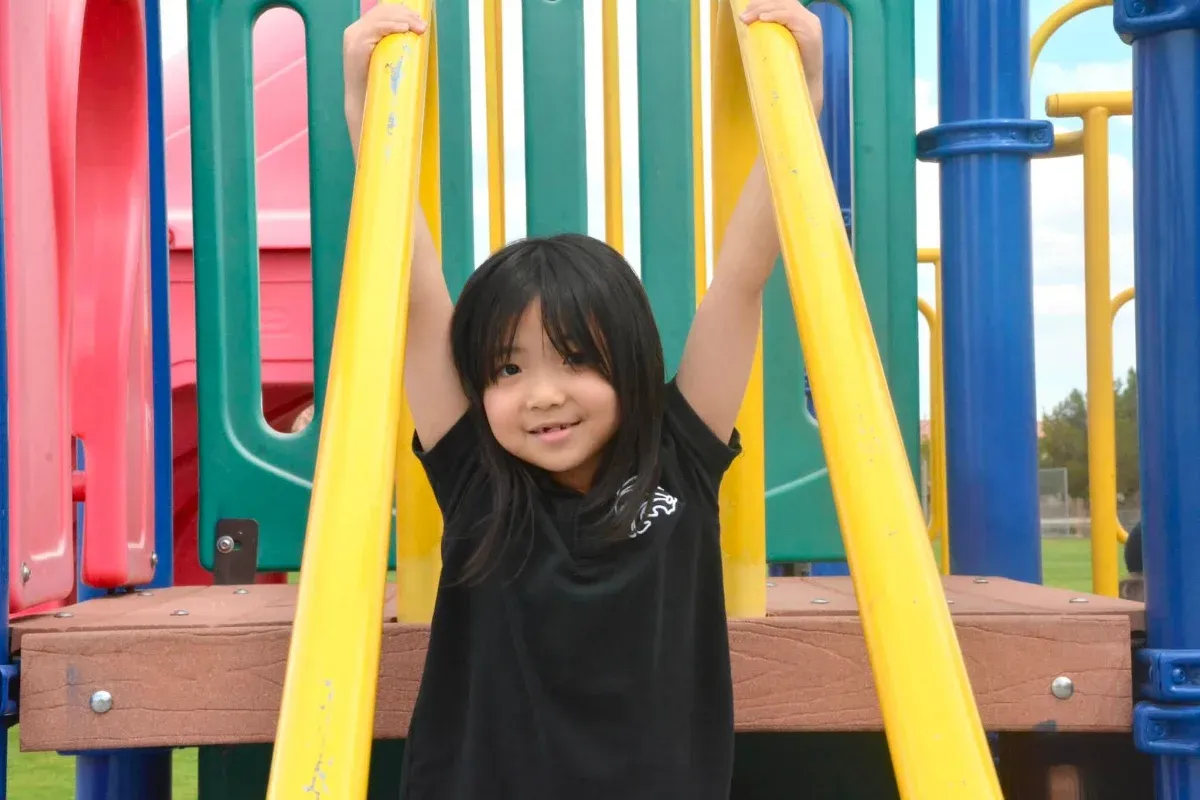 Smiling Awaken student hanging from the playground bars