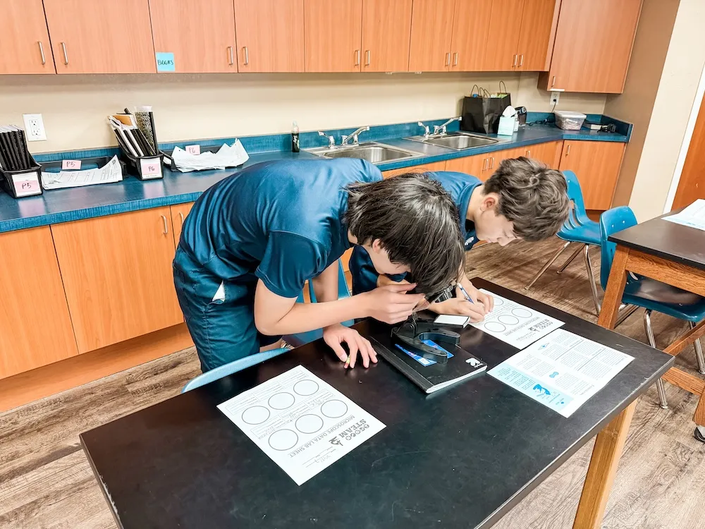Two middle school students looking through a microscope during a STEAM lab